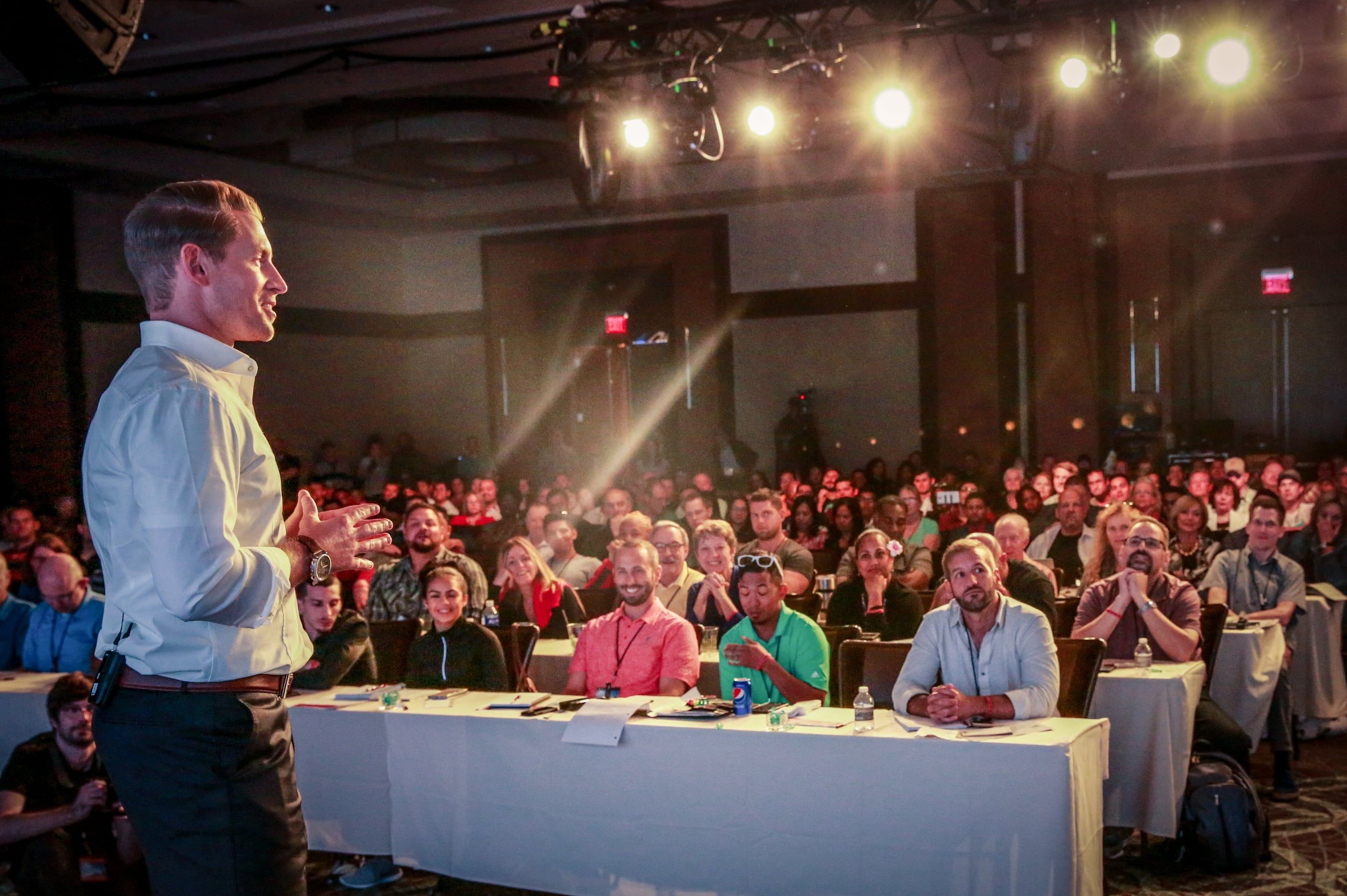 Jeremy Miner addressing a large seated audience at long tables